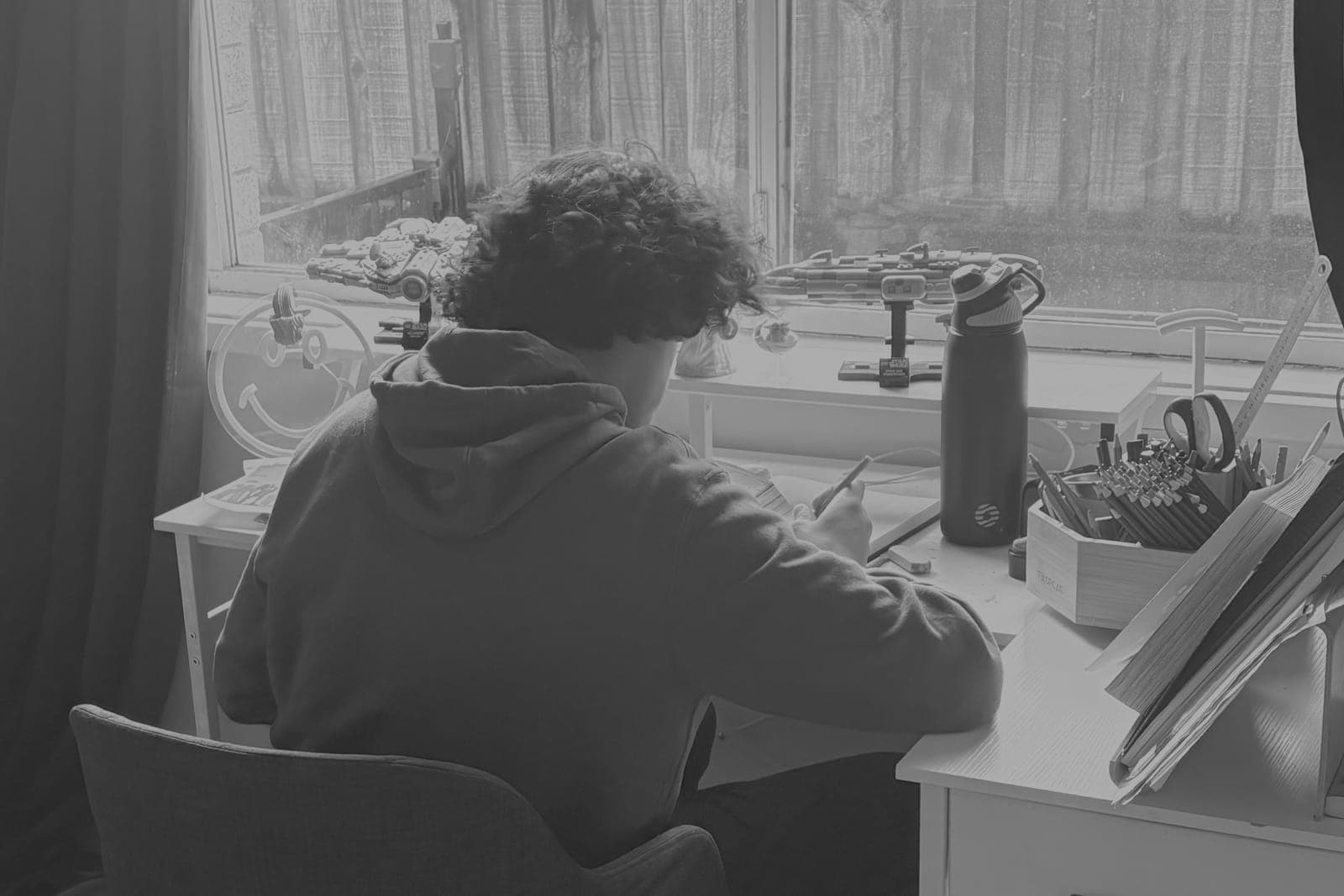A teenager drawing at a desk by a window